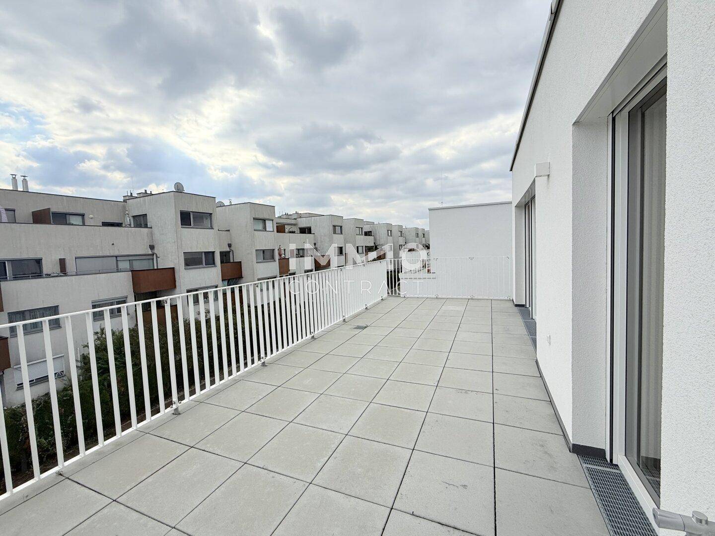 Weitläufige Dachterrasse mit hellen Fliesen und weißem Geländer, bietet viel Platz im Freien.