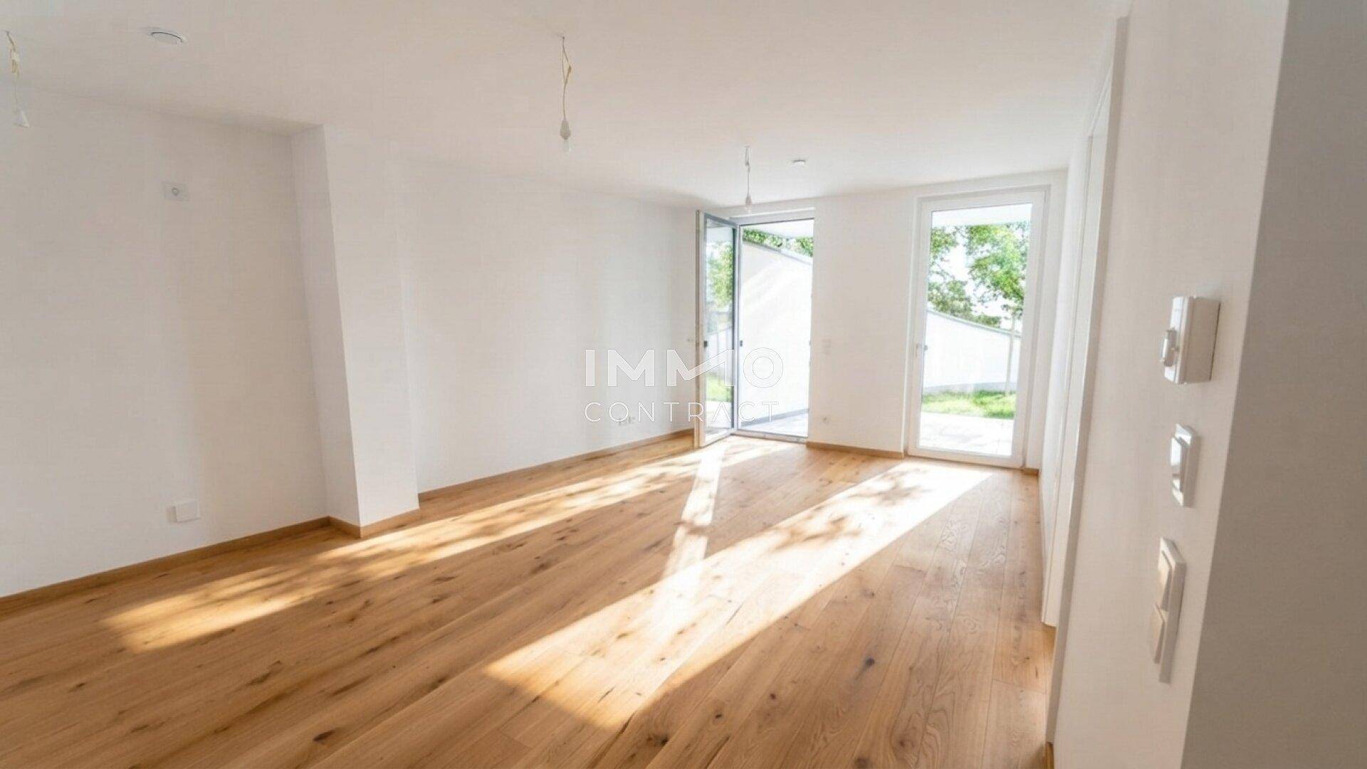 Heller, leerer Raum mit Eichenparkettboden und großen Glastüren, die viel Tageslicht hereinlassen.