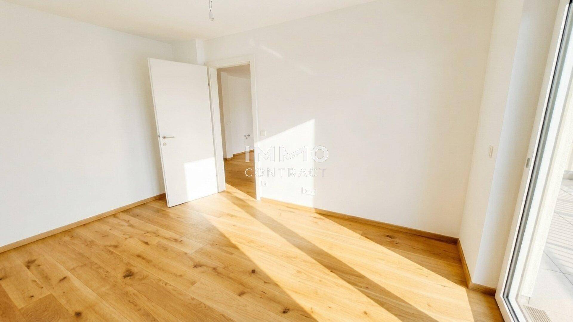Helles, leeres Zimmer mit Holzboden und Zugang zu einem Balkon oder einer Terrasse.