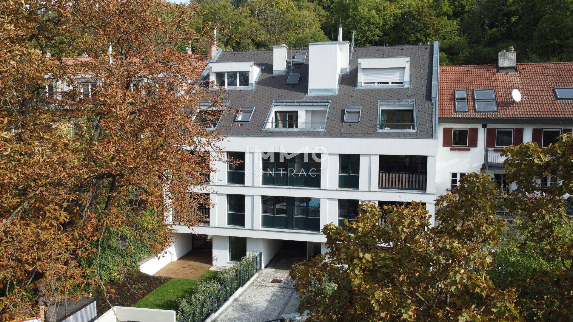 Moderne Wohnanlage mit mehreren Etagen und Dachschrägen, umgeben von Bäumen in herbstlicher Färbung.
