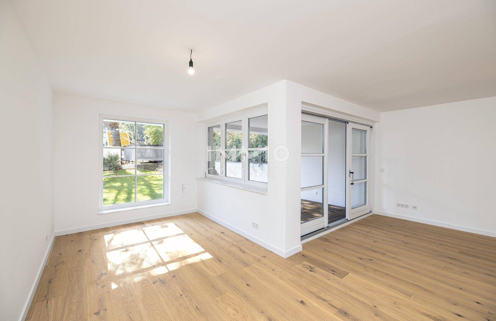 Lichtdurchfluteter Wohnraum mit Holzboden, großen Fenstern und Schiebetüren zum Außenbereich.