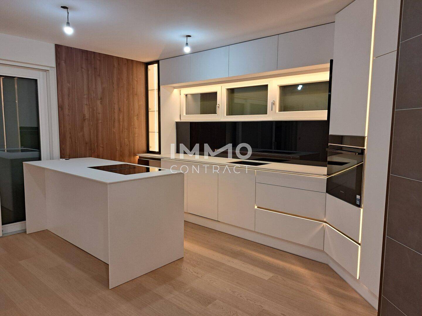 Moderne Küche mit weißer Kücheninsel, integrierten Geräten und Holzvertäfelung an der Wand.