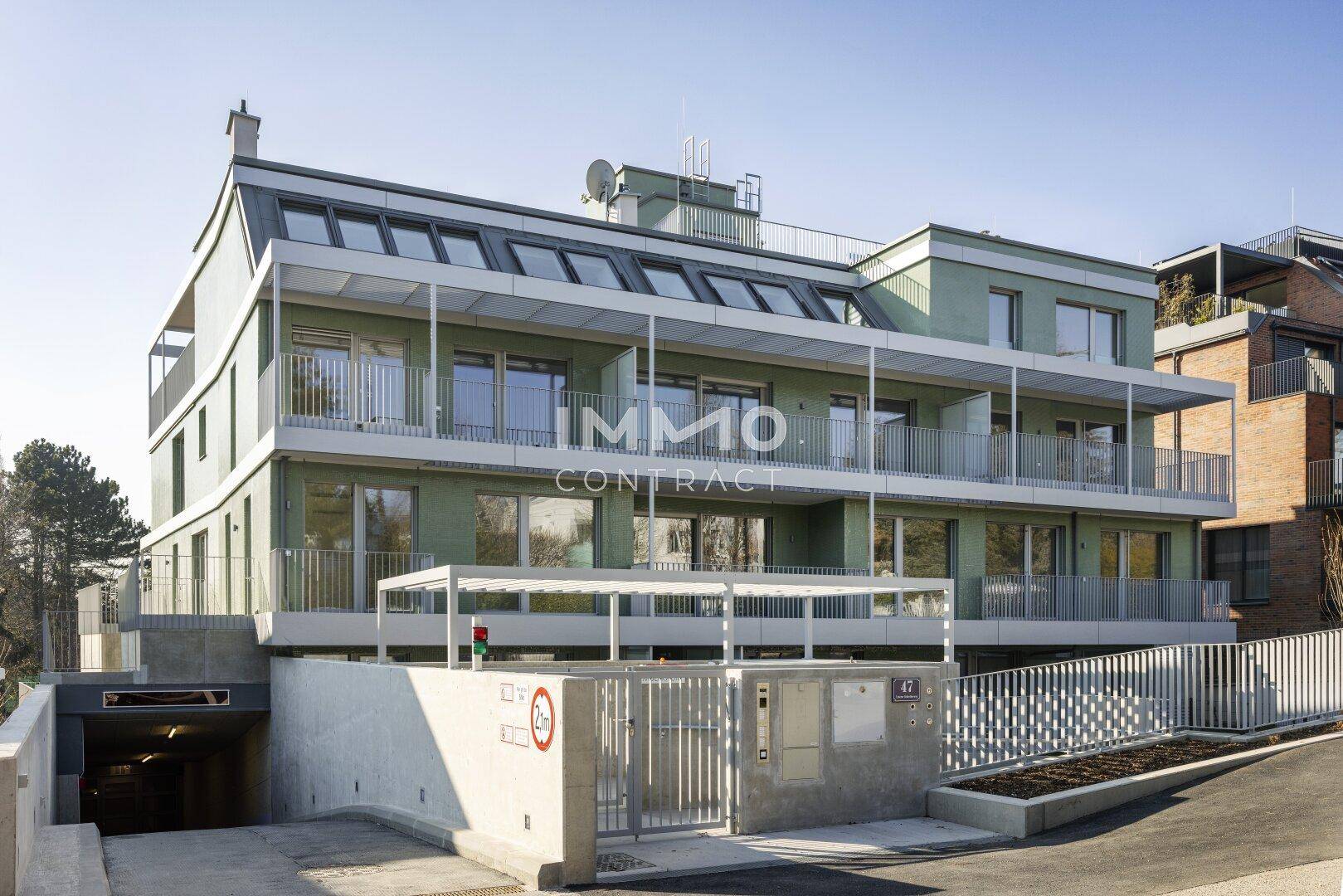 Modernes Wohngebäude mit grüner Fassade, Balkonen und Zufahrt zur Tiefgarage.