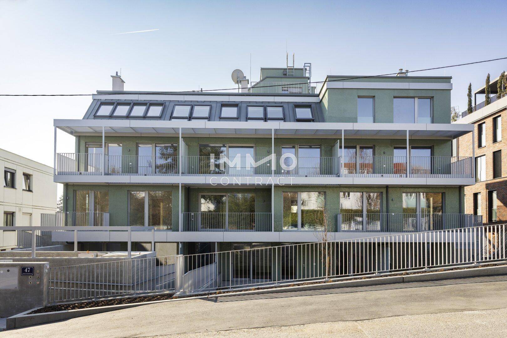 Moderne Wohnanlage mit mehreren Balkonen und Dachfenstern unter blauem Himmel.