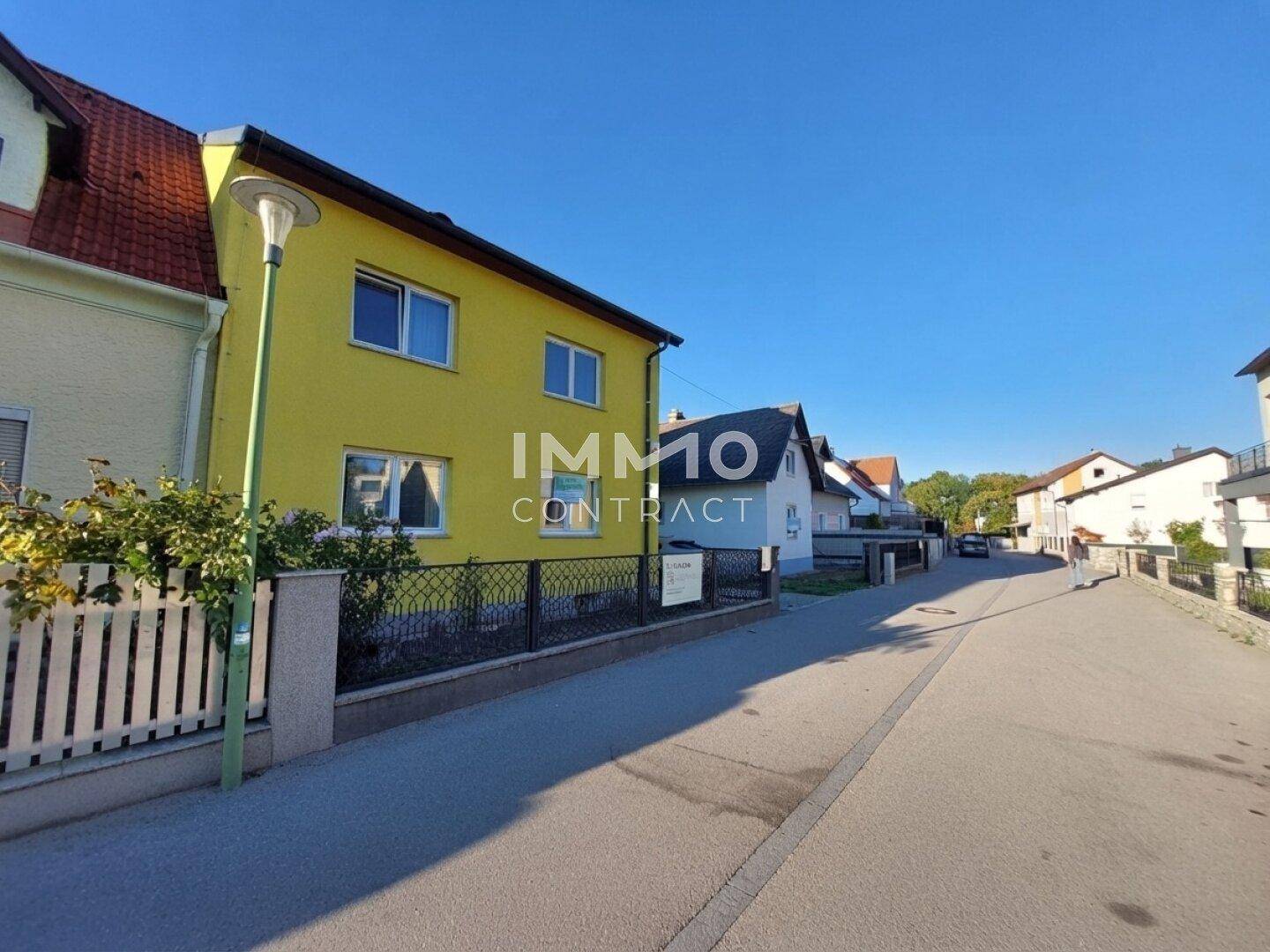 Ansicht des gelben Hauses von der Straße mit Zaun und klarem blauen Himmel.