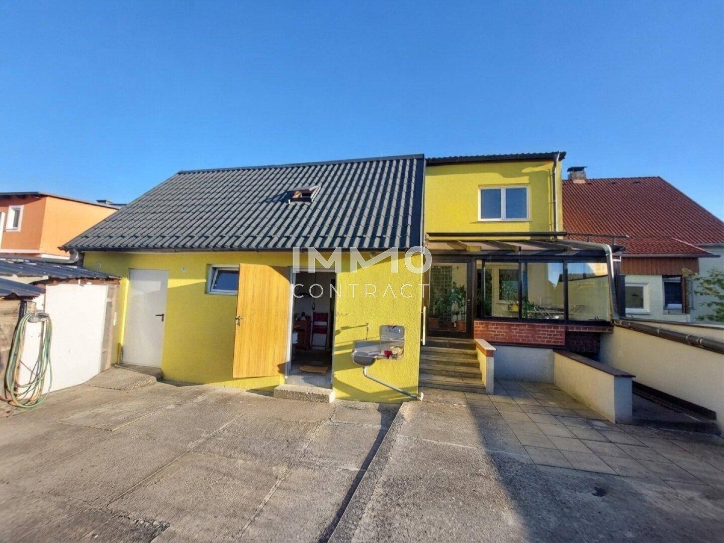 Rückseite des gelben Hauses mit Wintergarten und gepflastertem Hofbereich.