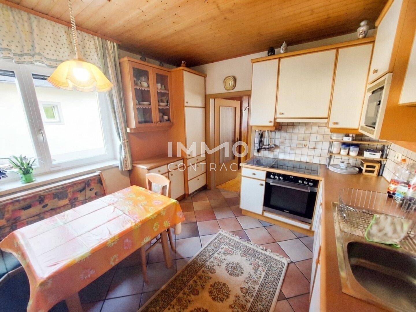 Gemütliche Küche mit Holzbalkendecke, gefliestem Boden und Essbereich am Fenster.