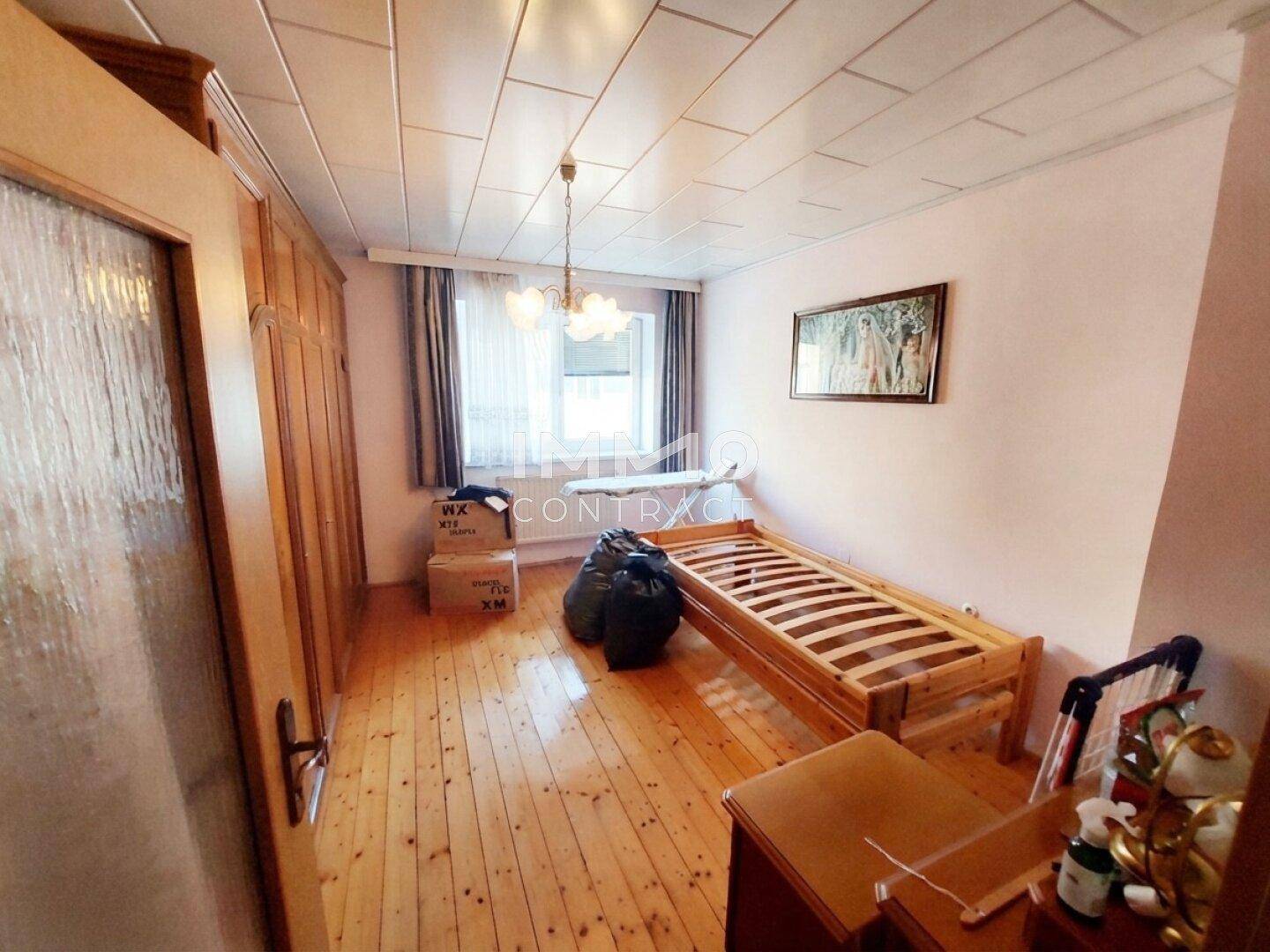 Schlafzimmer mit Holzfußboden, Holzdecke und einem Einzelbett am Fenster.