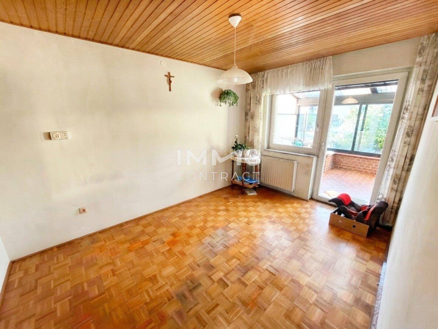 Heller Wohnraum mit Parkettboden, Holzdecke und Zugang zu einem verglasten Wintergarten.