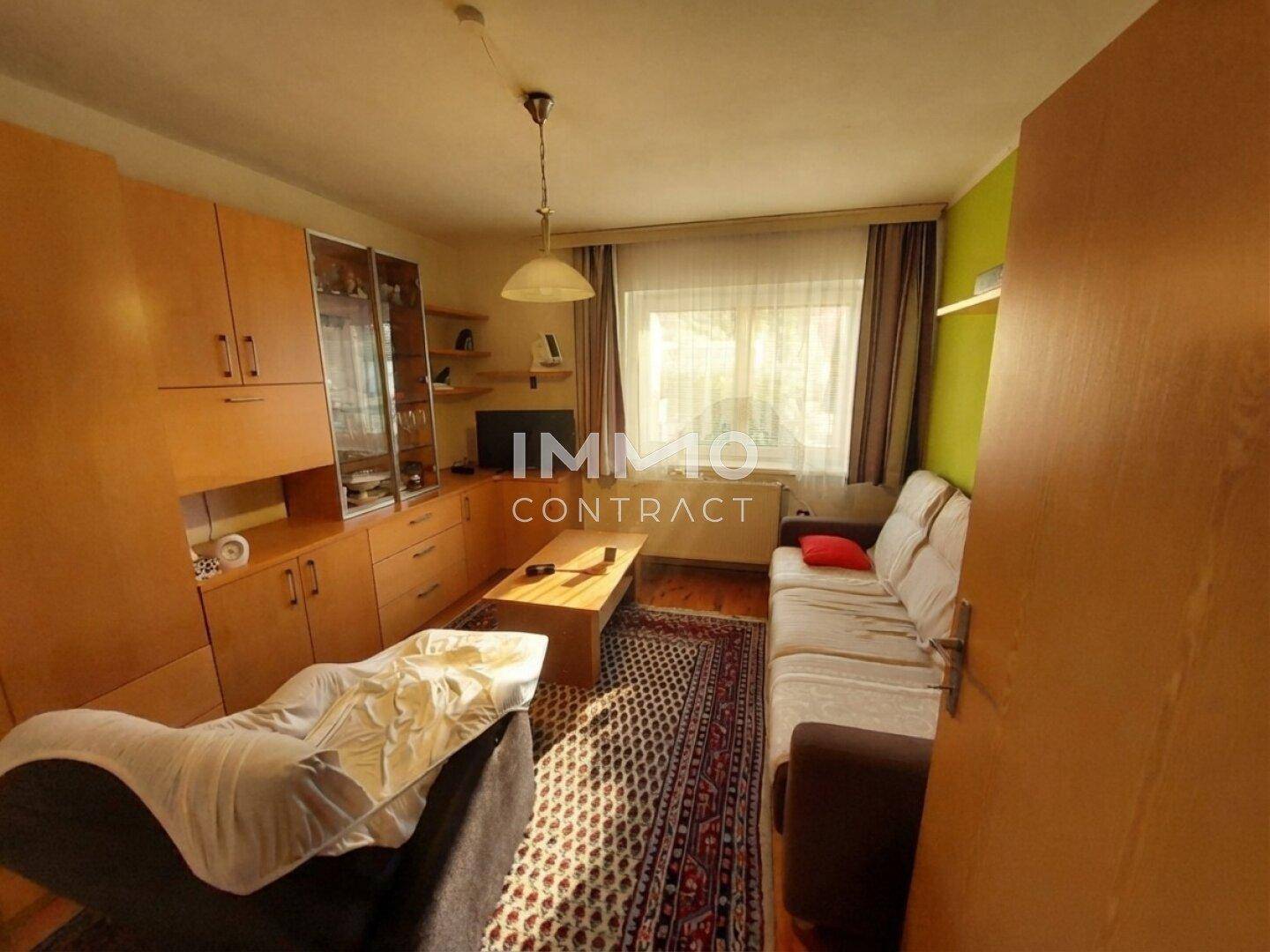 Wohnzimmer mit Sofa, Teppich und Holzmöbeln unter einer Holzdecke.