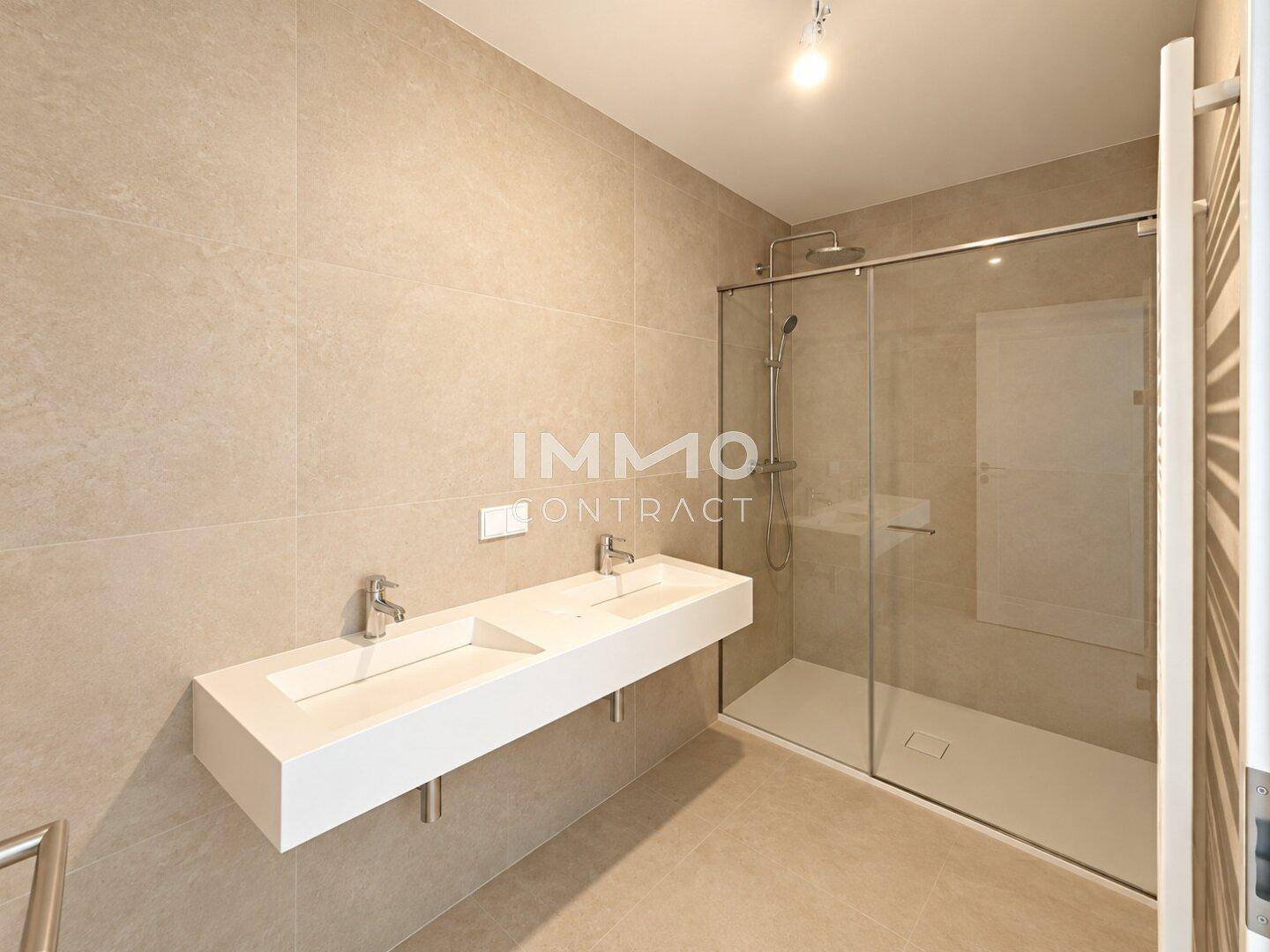 Modernes Badezimmer mit Doppelwaschbecken, großer begehbarer Dusche und hellen Fliesen.