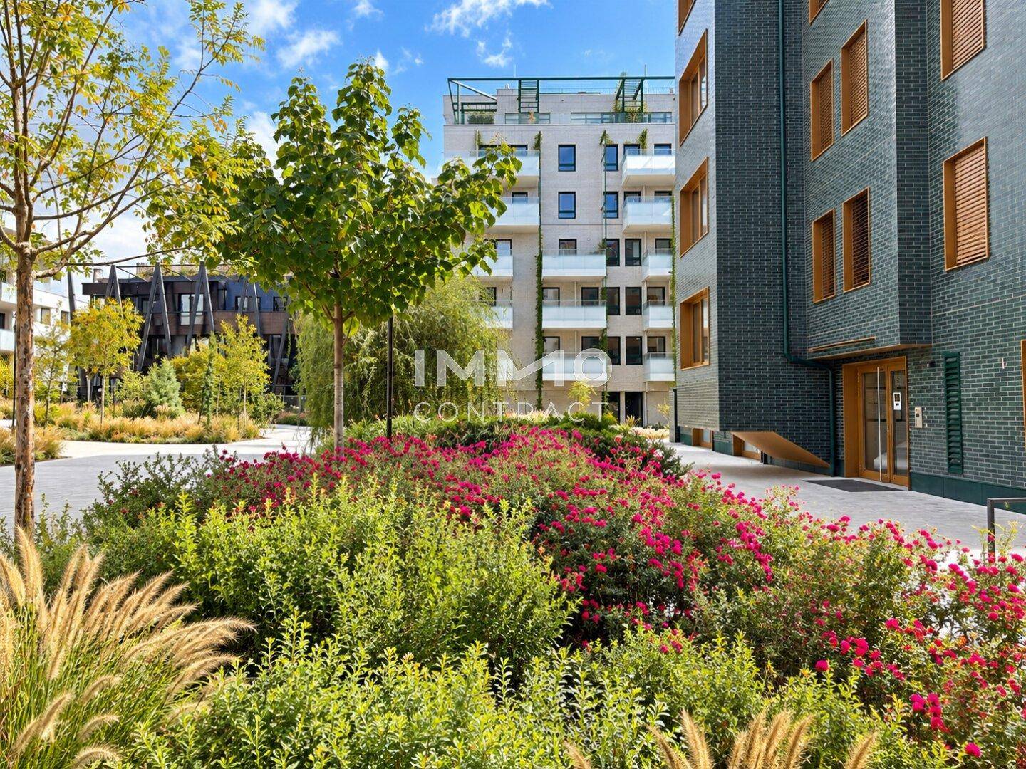 Gepflegte Gartenanlage mit blühenden Sträuchern und Bäumen vor einem modernen Wohngebäude.