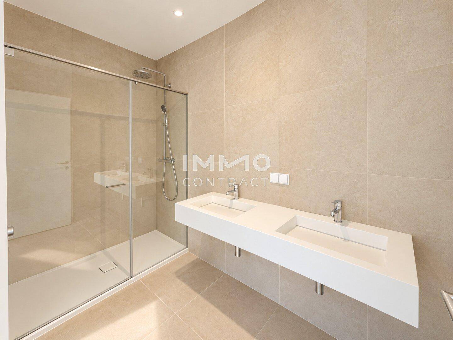 Modernes Badezimmer mit doppelten Waschbecken, großer begehbarer Dusche und hellen Fliesen.