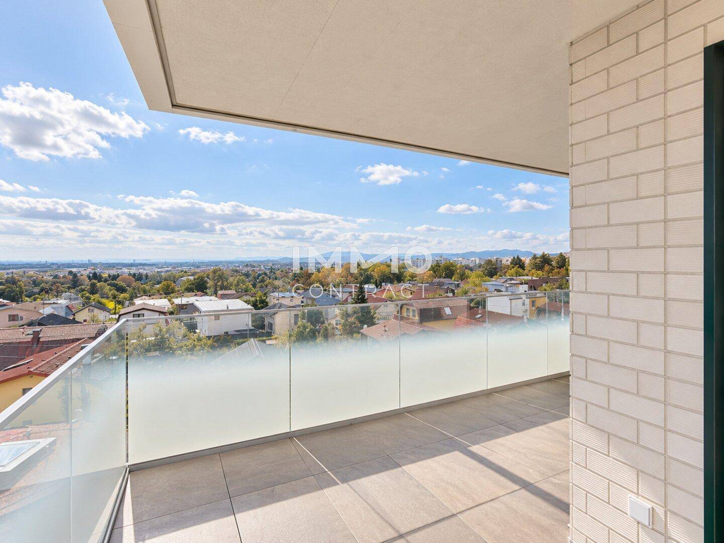 Breiter Balkon mit Fliesenboden und Glasbrüstung, bietet einen Panoramablick über die Umgebung.