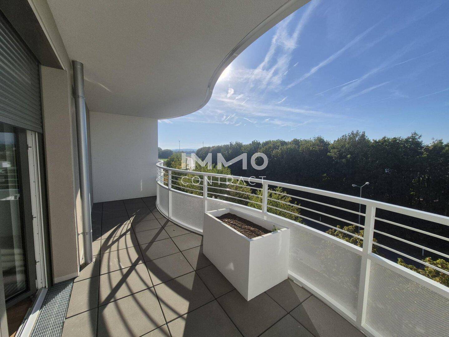 Geräumiger Balkon mit Fliesenboden, weißem Geländer und weitem Blick ins Grüne.