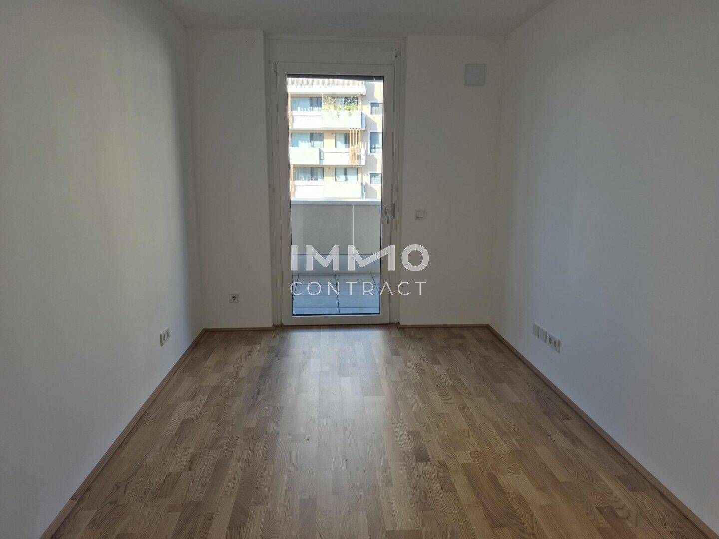 Helles Schlafzimmer mit Parkettboden und Zugang zu einem französischen Balkon.