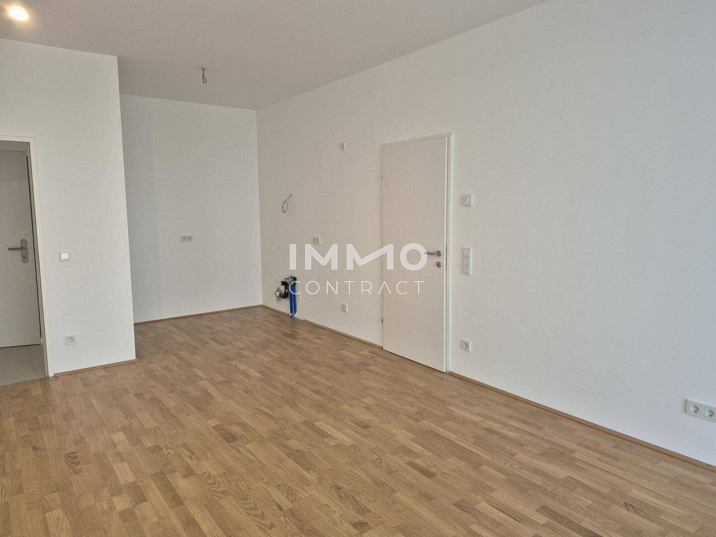 Leerer Raum mit Parkettboden und Anschlüssen für eine zukünftige Küche.