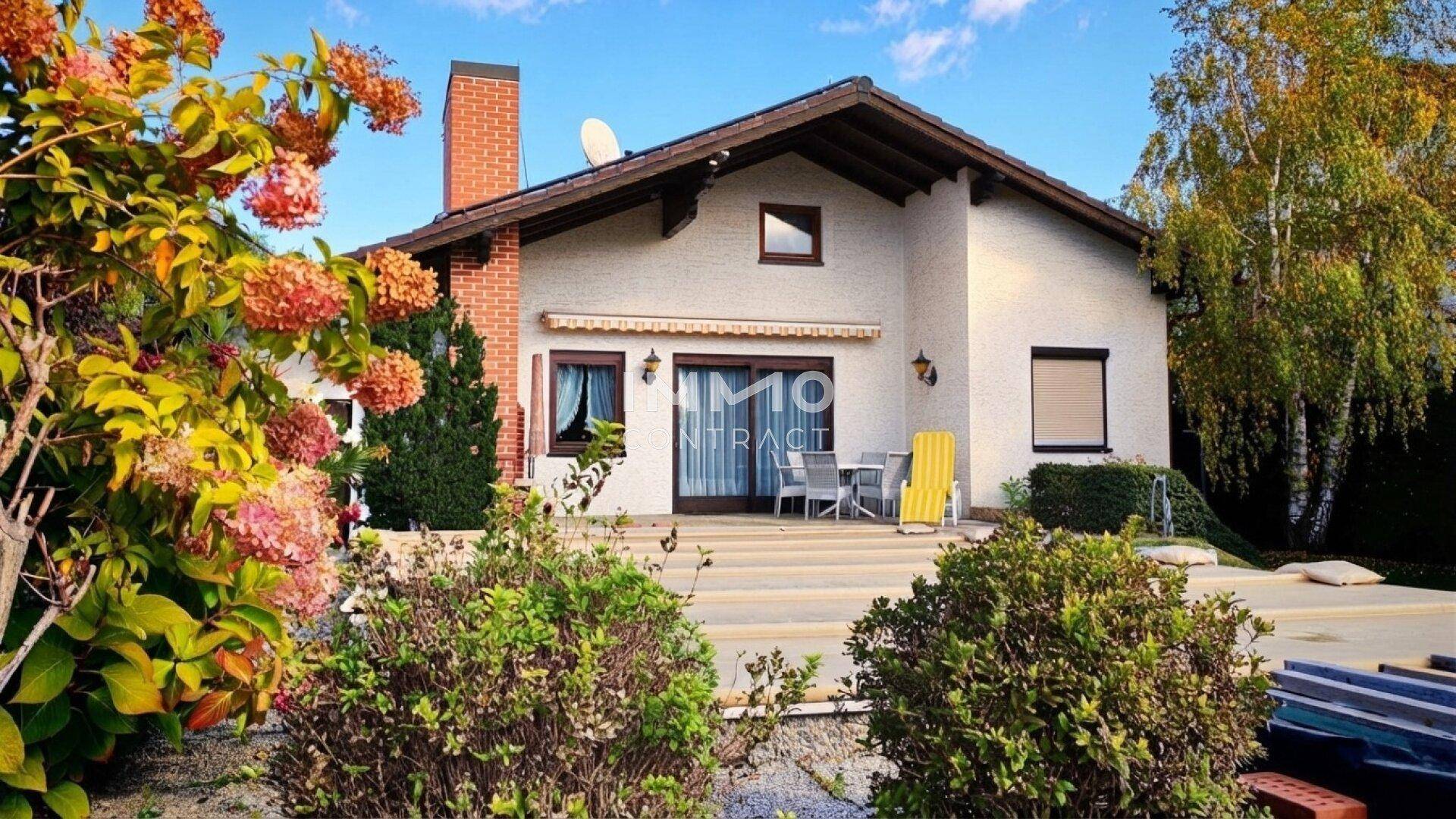 Hausansicht vom Garten aus mit blühenden Sträuchern und Terrasse.