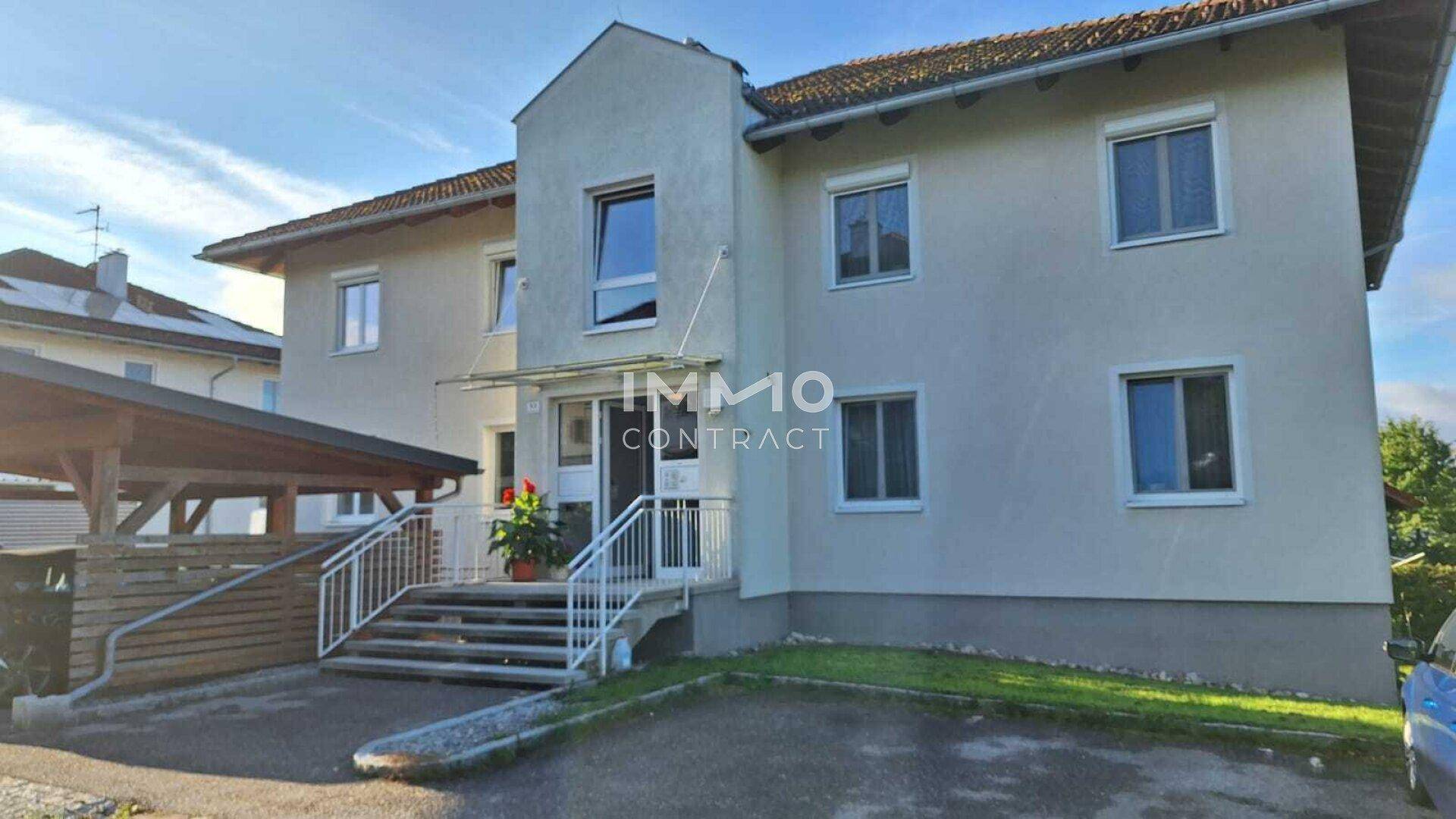 Vorderansicht eines Mehrfamilienhauses mit Eingangsbereich, Treppe und überdachtem Carport.