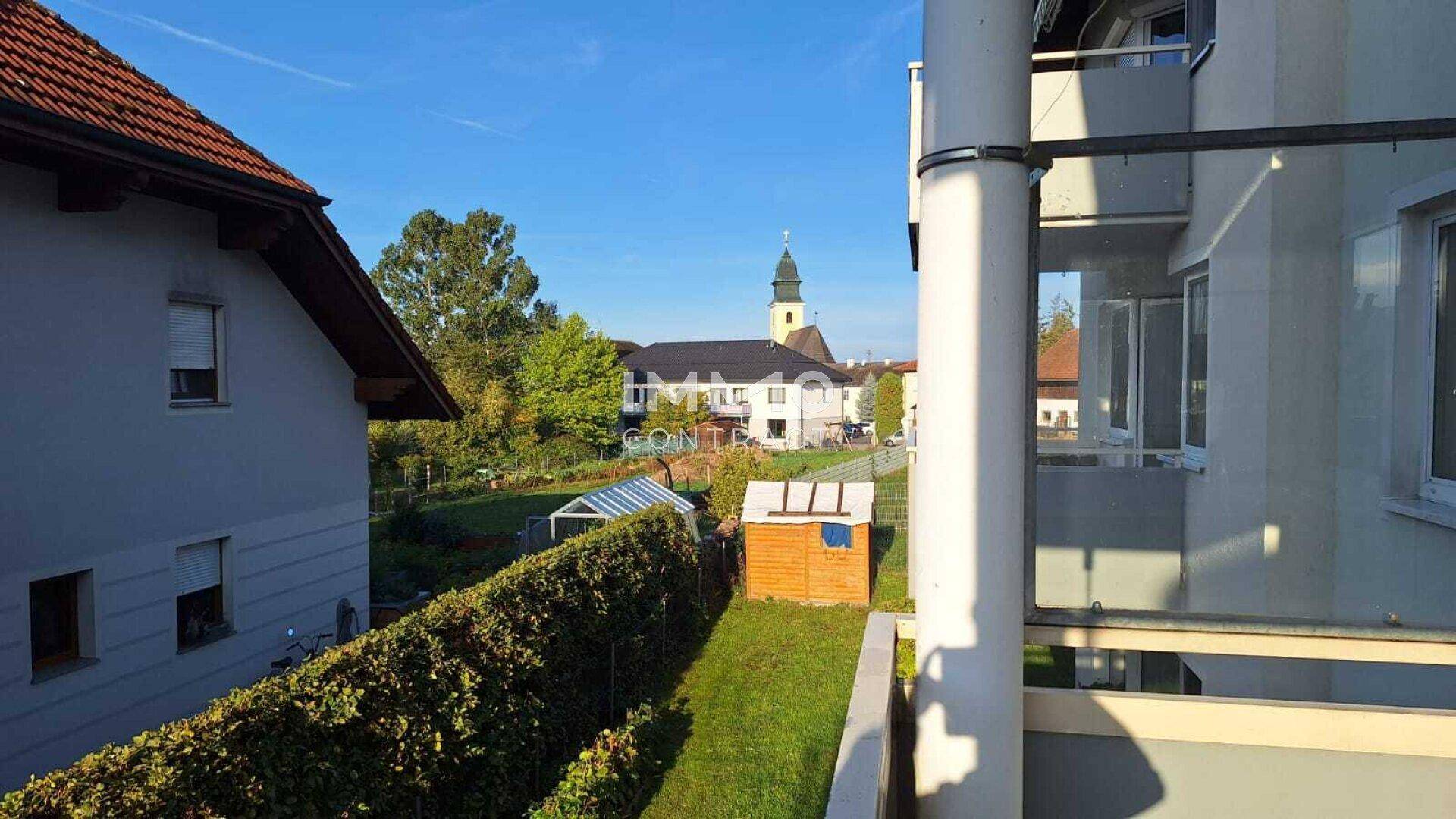 Blick von einem Balkon auf einen Garten, Nachbarhäuser und einen Kirchturm in der Ferne.