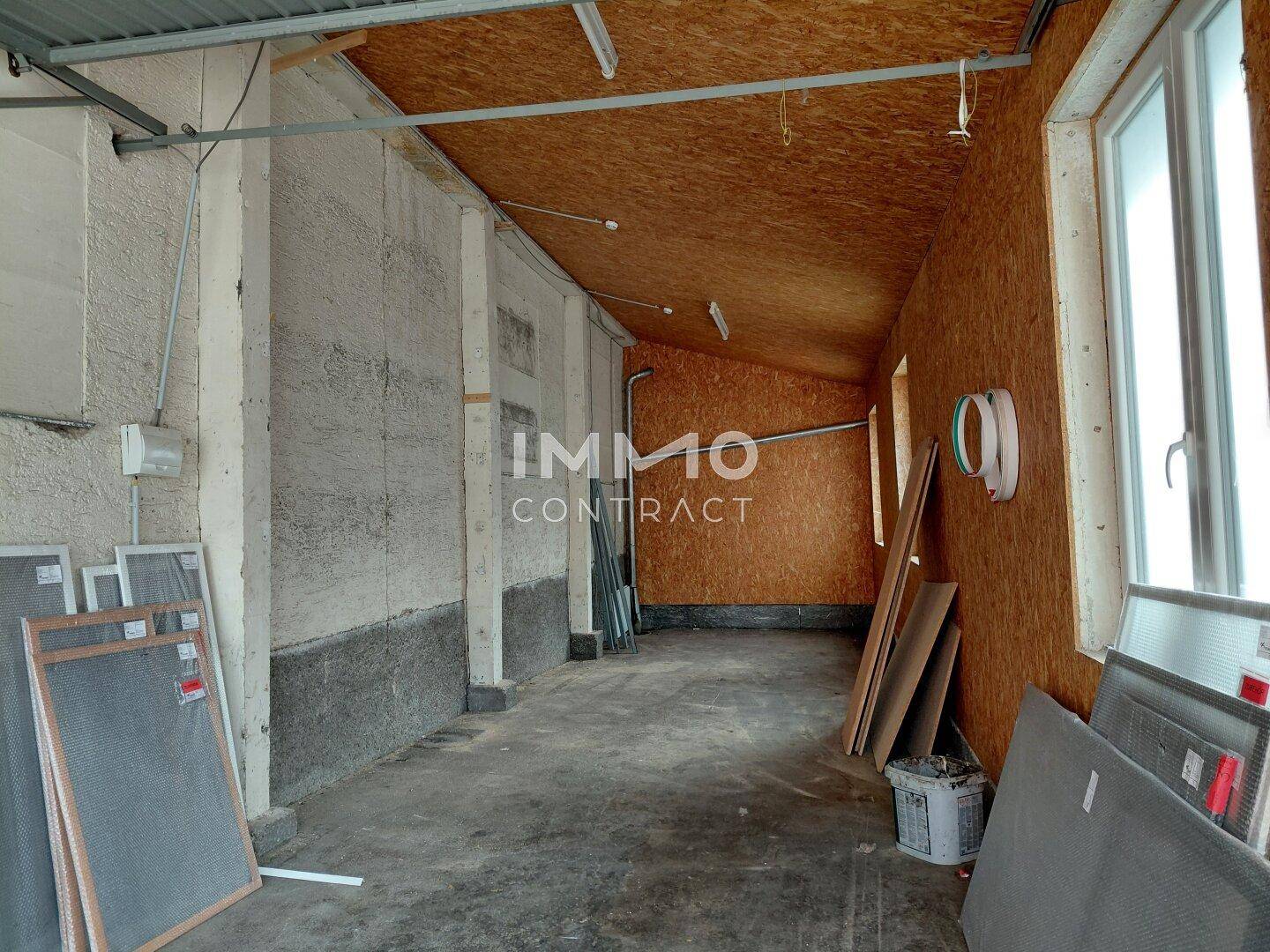 Geräumiger Innenraum mit Betonwänden, OSB-Decke und -Wand, sowie einem großen Fenster für Tageslicht.