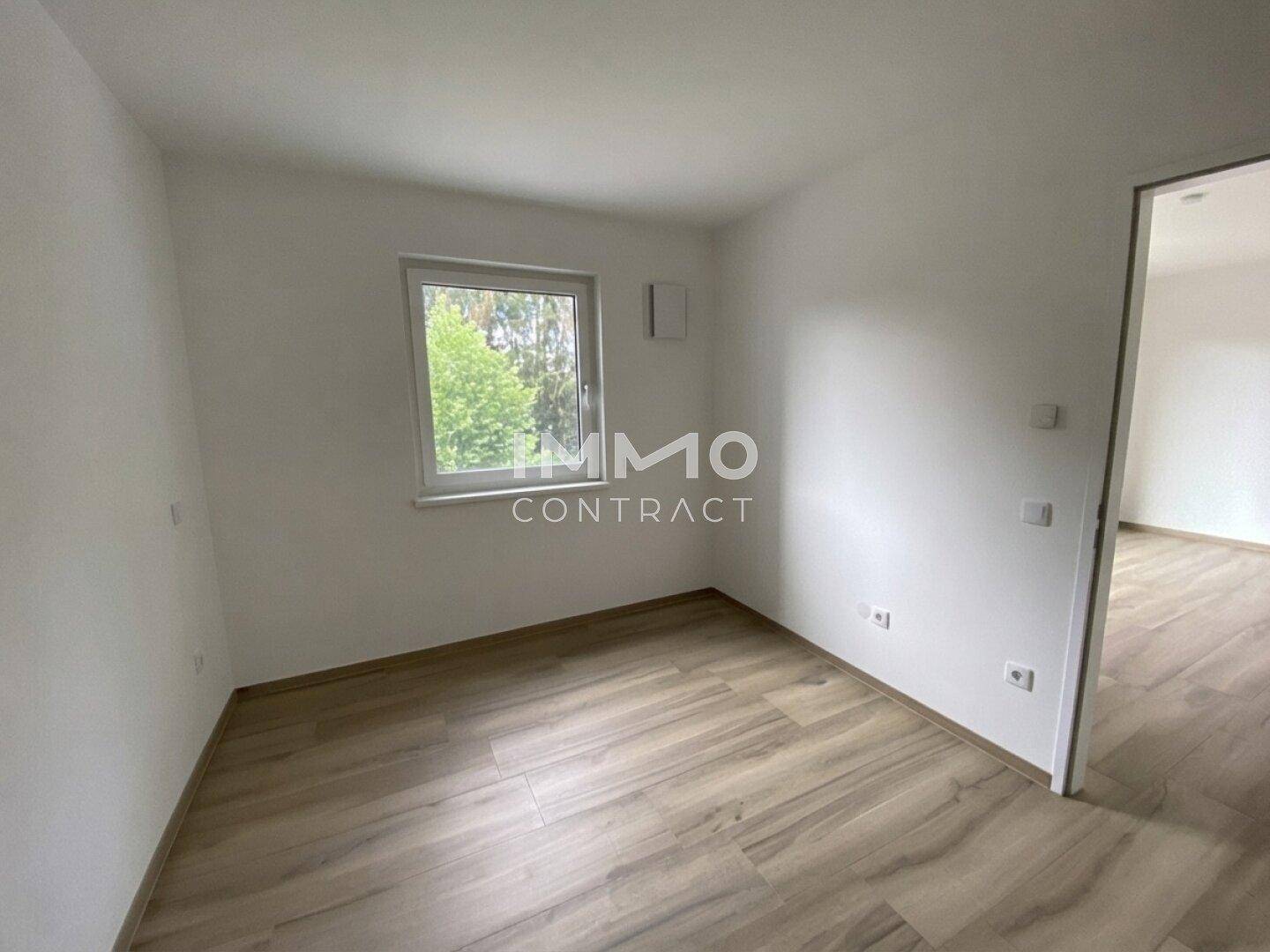 Leeres Zimmer mit Laminatboden und Fenster, bereit zur individuellen Gestaltung.