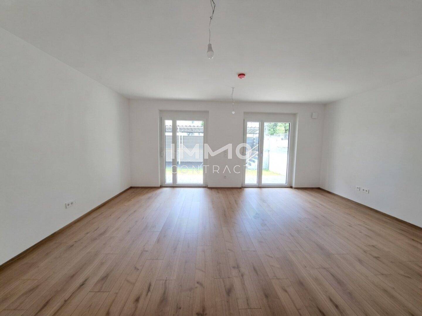 Heller, leerer Raum mit Holzboden und großen Fenstern, bereit zum Einzug.
