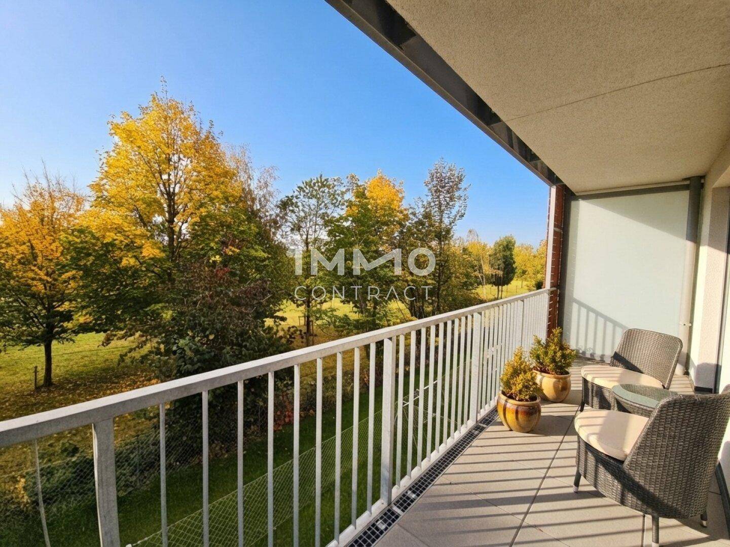 Geräumiger Balkon mit Sitzgelegenheiten und weitem Blick auf Bäume.