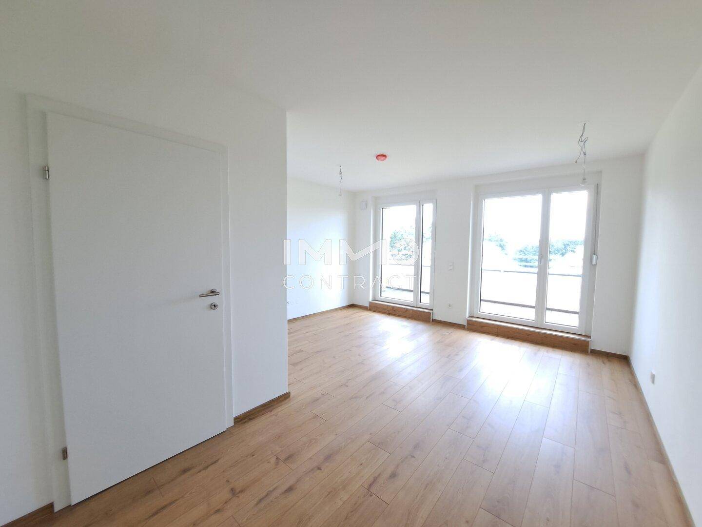 Heller, unmöblierter Raum mit Laminatboden und großen Fenstern.