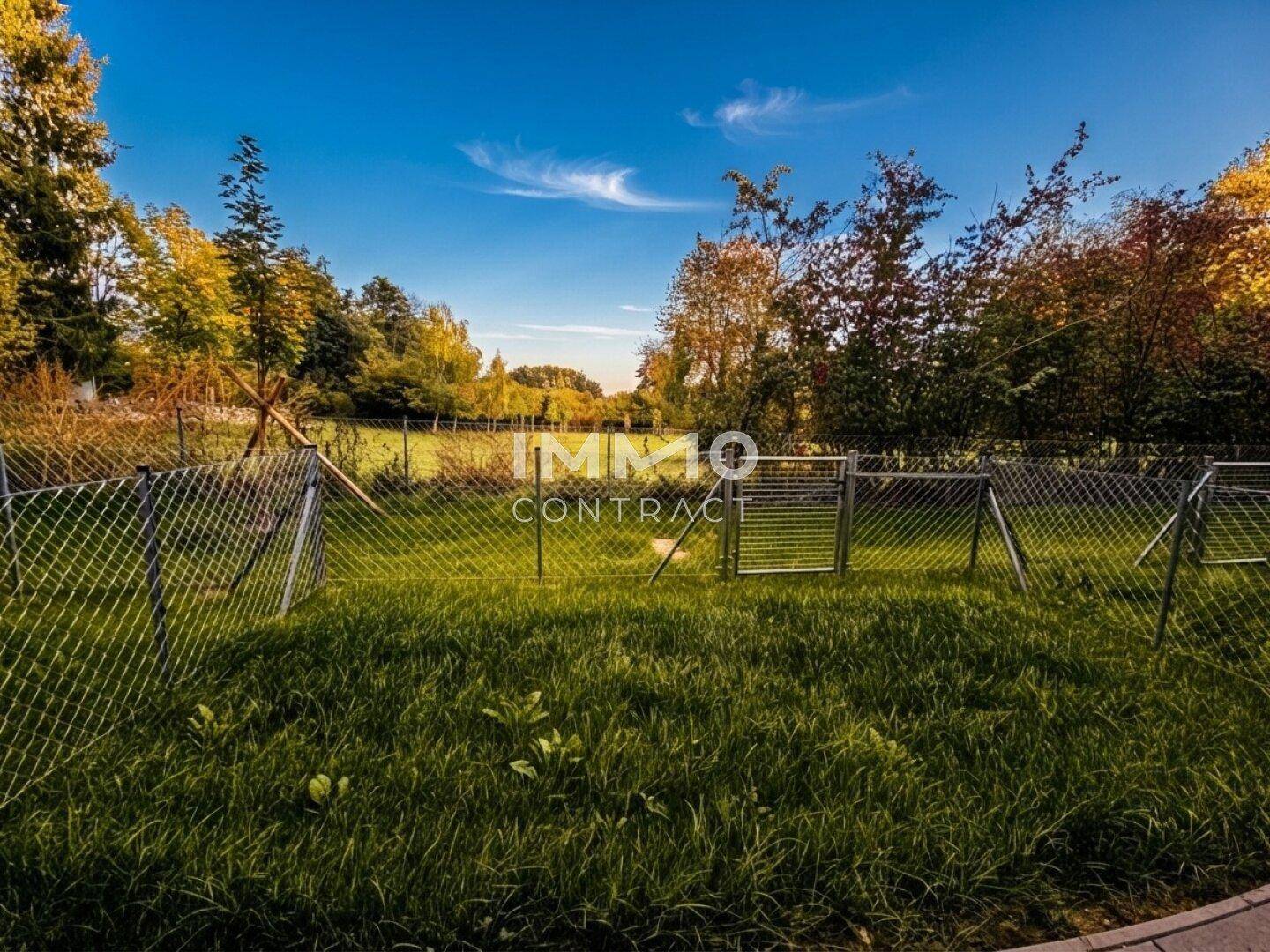 Eingezäunter Gartenbereich mit Rasenfläche und altem Baumbestand im Hintergrund der Wohnanlage.