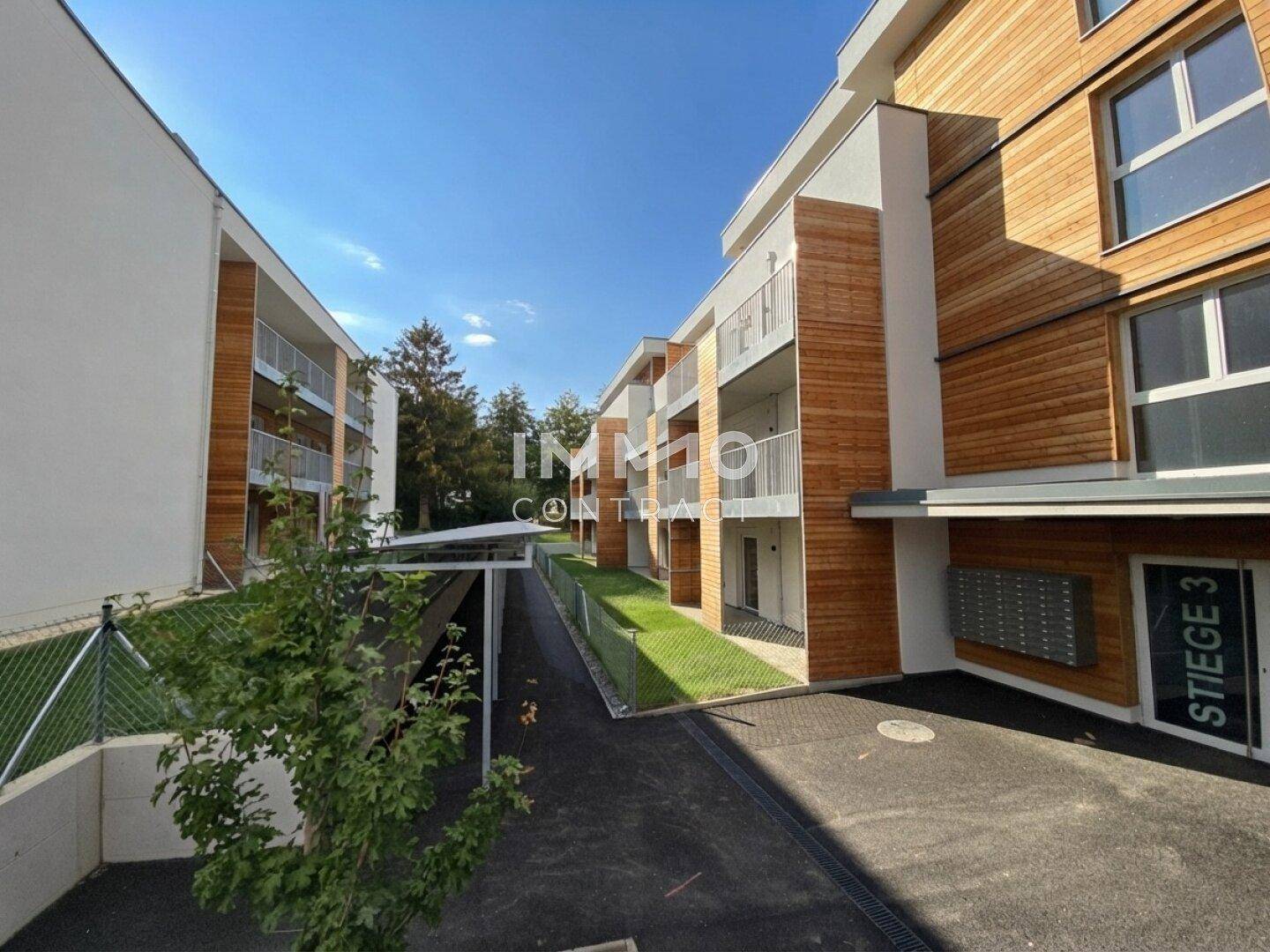 Moderne Wohnanlage mit Holzfassaden, Balkonen und gepflegten Außenbereichen unter blauem Himmel.