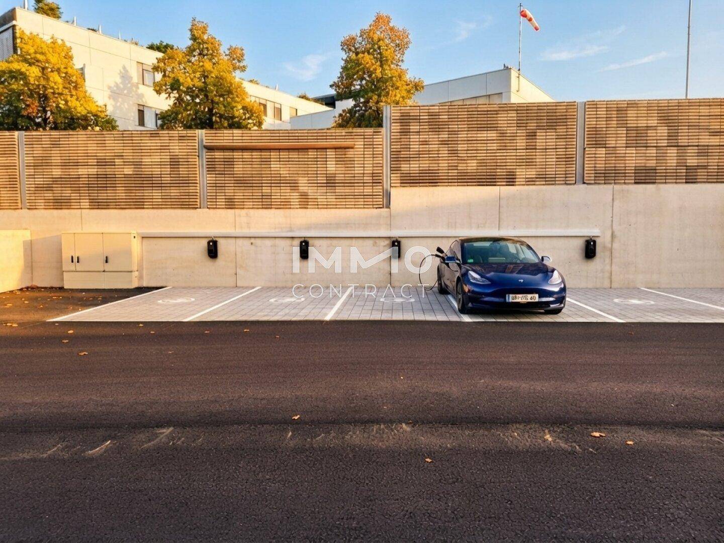 Außenparkplätze mit Ladestationen für Elektrofahrzeuge und einem geparkten blauen Auto.