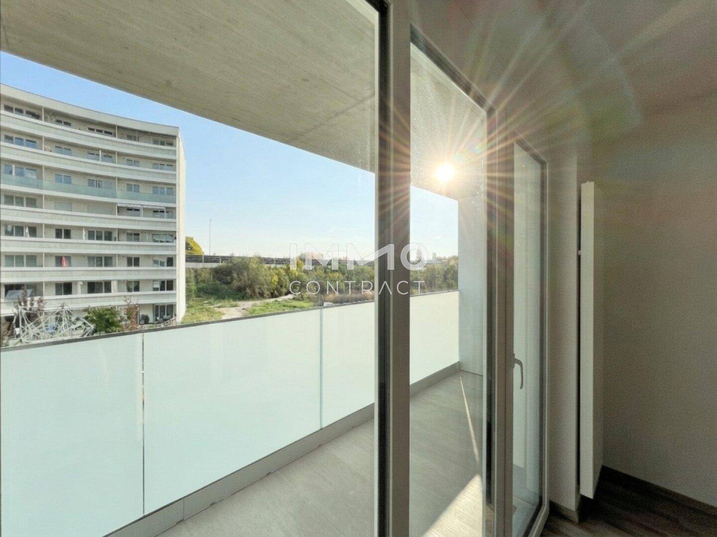 Sonniger Balkon mit moderner Glasbrüstung und urbanem Ausblick auf die umliegende Bebauung.