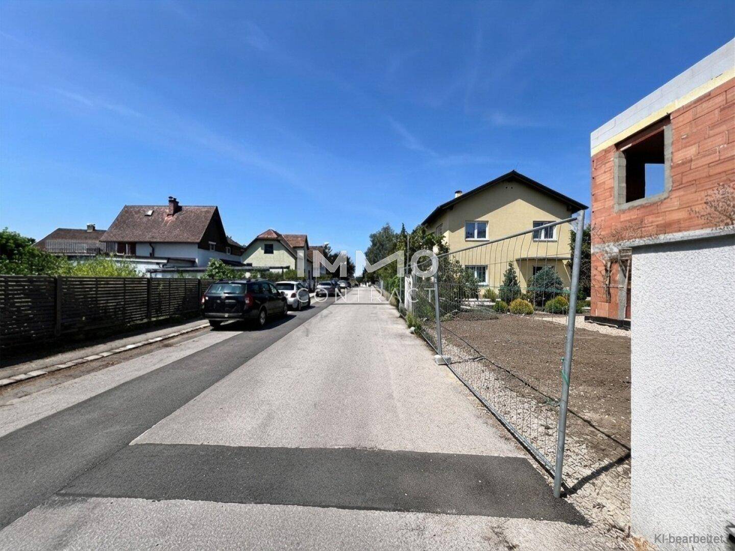 Blick auf die ruhige Wohnstraße mit dem im Bau befindlichen Doppelhaus und umliegender Natur.