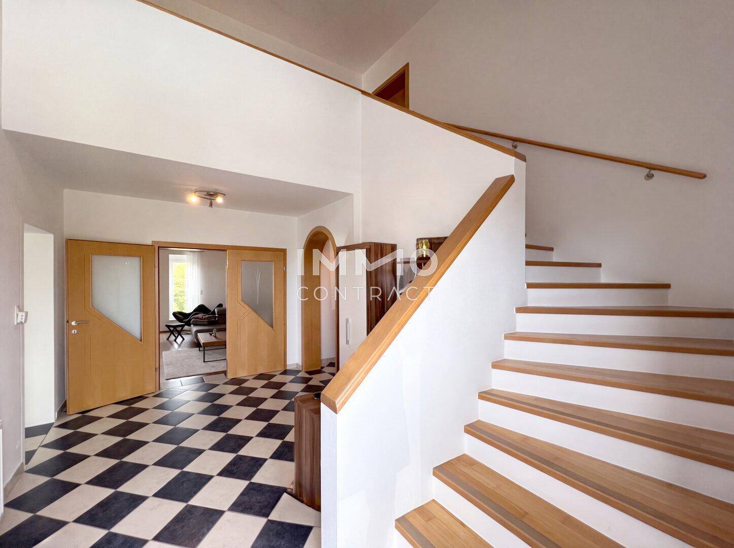 Geräumiger Flur mit Schachbrettmuster-Fliesenboden und Holztreppe zum Obergeschoss.
