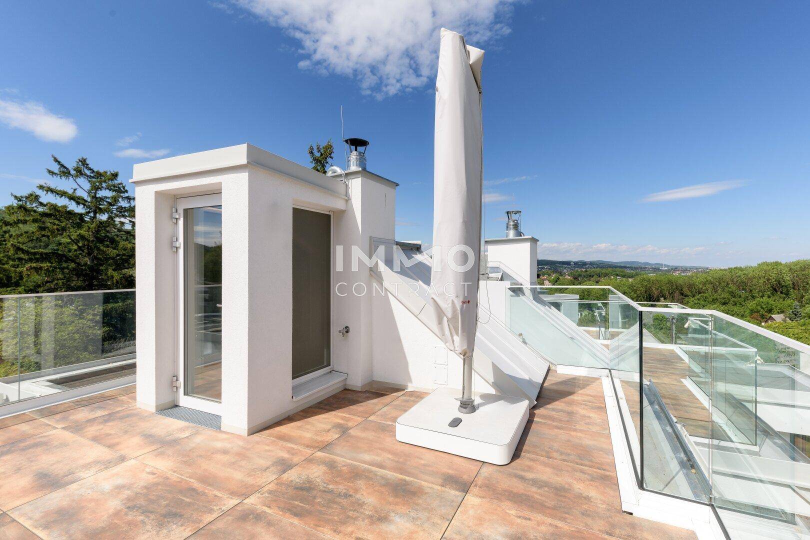 Geräumige Dachterrasse mit Sonnenschirm und Zugang zu einem Dachaufbau.