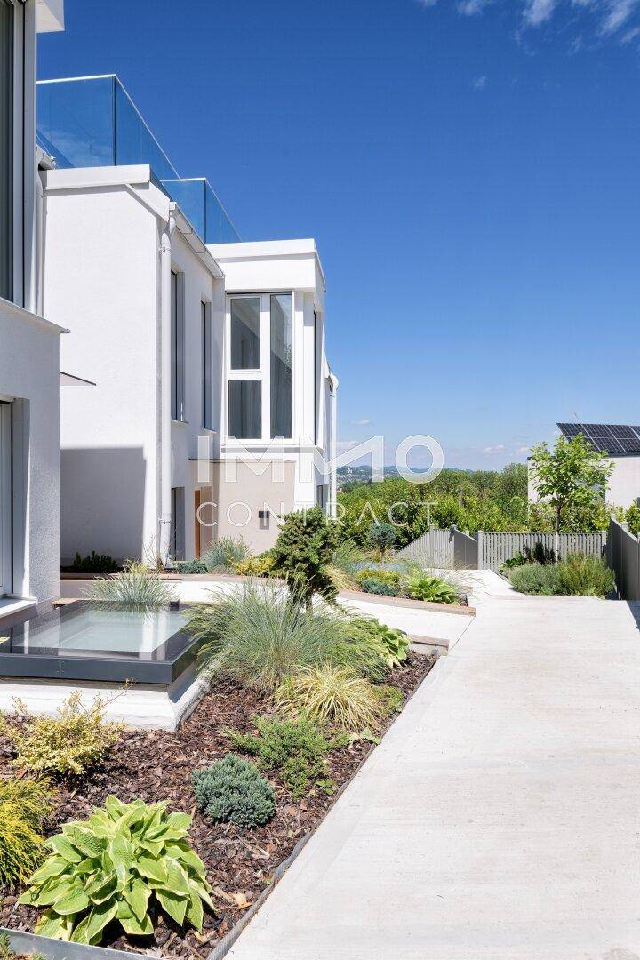 Gepflegter Gartenbereich mit verschiedenen Pflanzen und modernem Gebäude im Hintergrund.