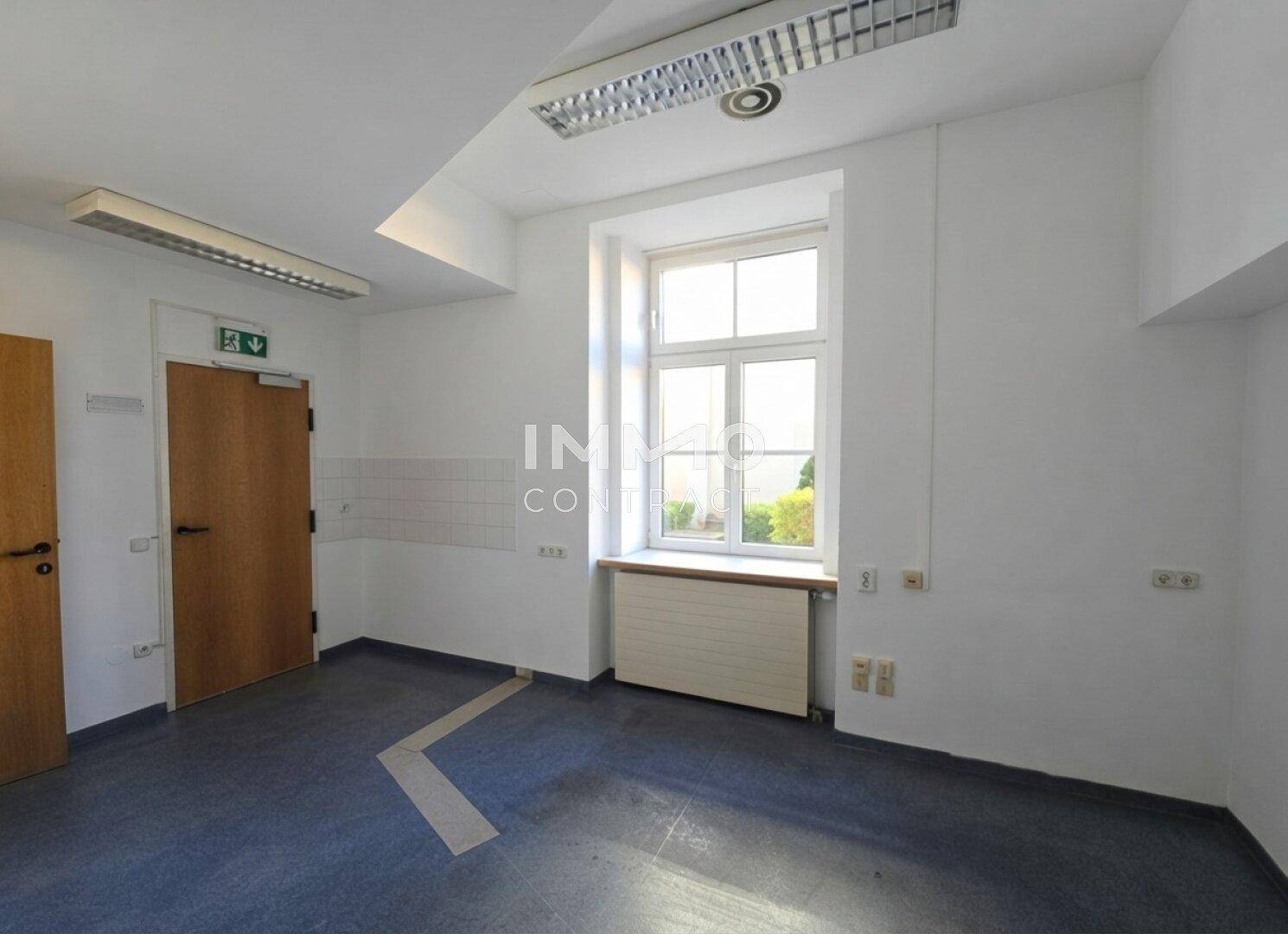 Funktionaler Raum mit dunklem Boden, weißen Wänden und einem Fenster, geeignet für Bürozwecke.