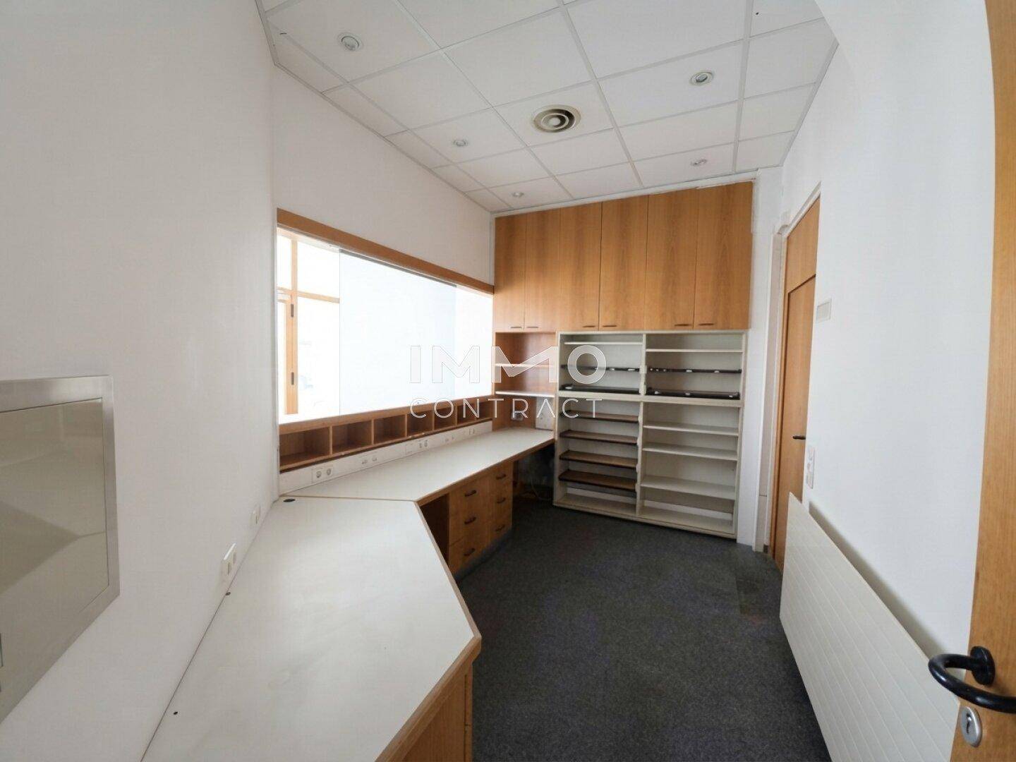 Büroraum mit Teppichboden, Einbauschränken und einem langen Schreibtisch, bietet viel Stauraum.