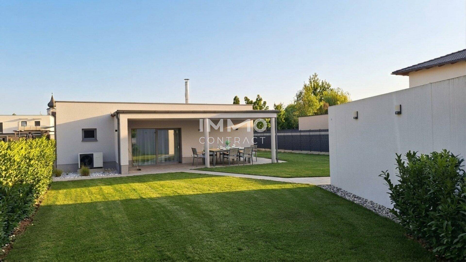 Rückseite des modernen Hauses mit weitläufigem Garten und überdachter Terrasse für Mahlzeiten im Freien.