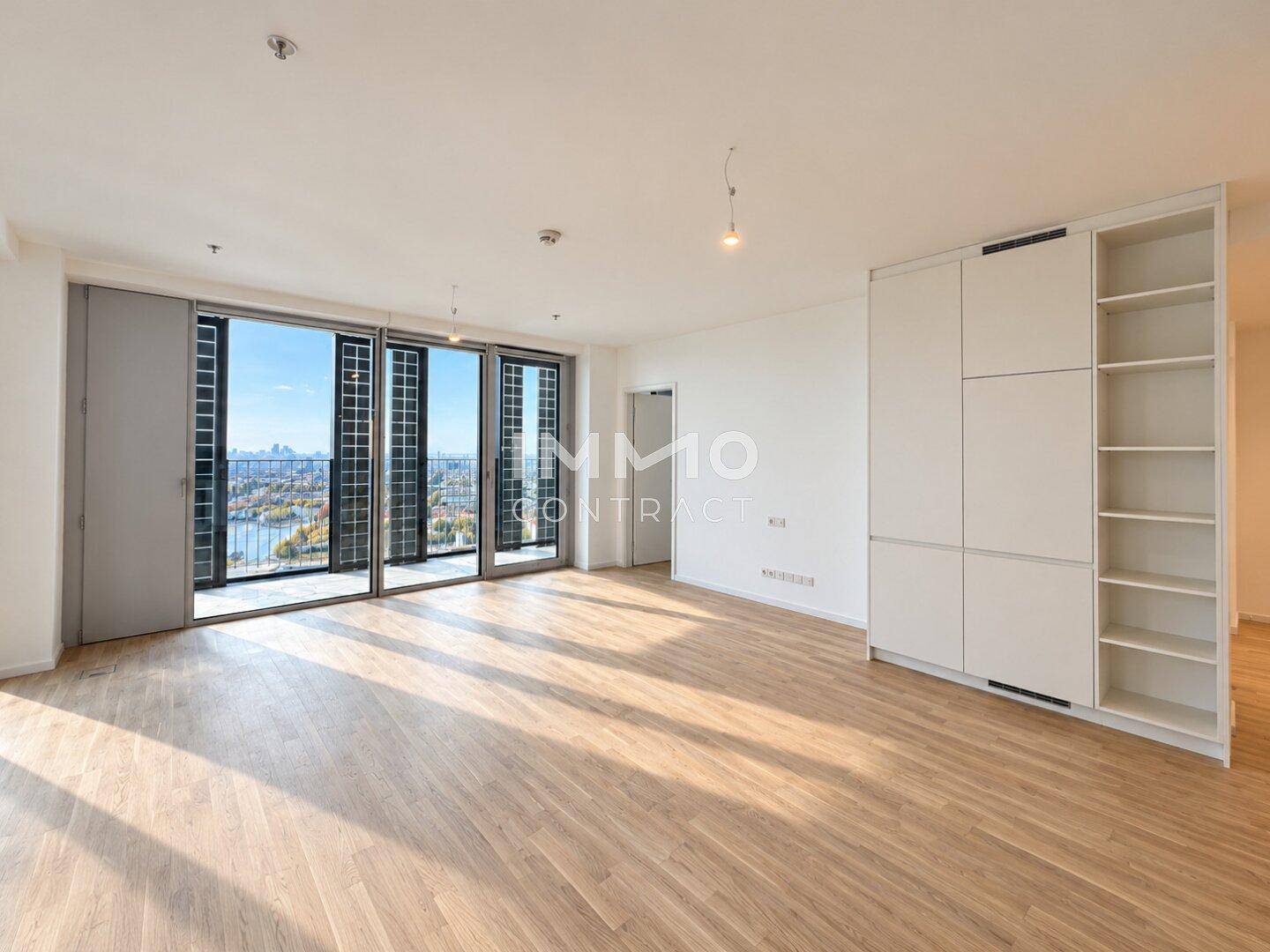 Heller Wohnraum mit Holzboden und integrierten Schränken, der Zugang zu einem Balkon bietet.