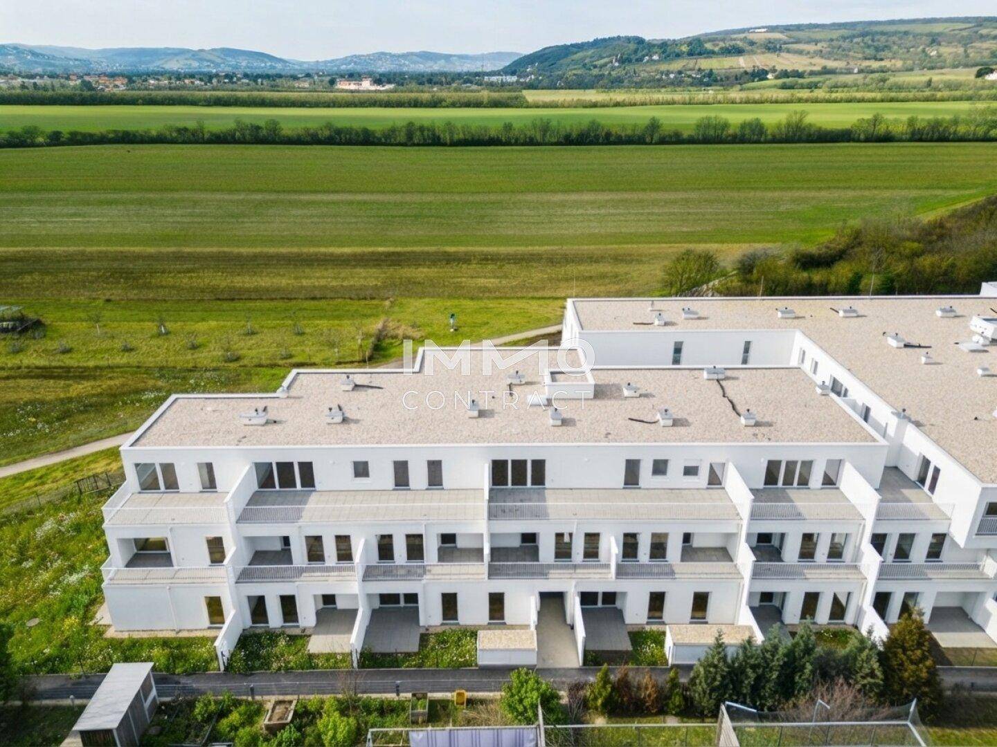 Moderne Wohnanlage mit weißer Fassade, umgeben von grünen Feldern und Hügeln.