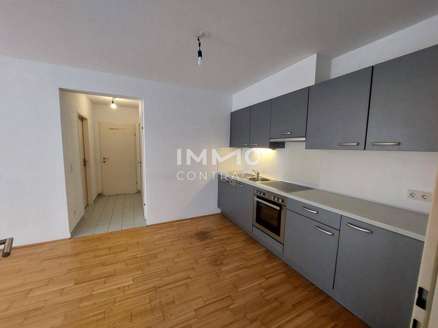 Moderne Küche mit grauen Schränken, integrierten Geräten und Parkettboden, offen zum Flur.