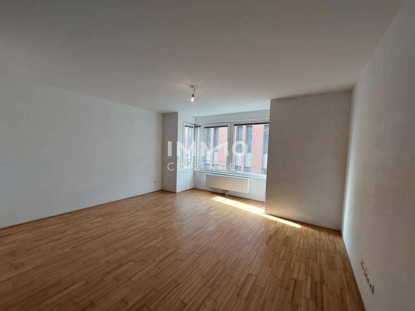 Geräumiges, unmöbliertes Wohnzimmer mit hellem Parkettboden und einem Erkerfenster.