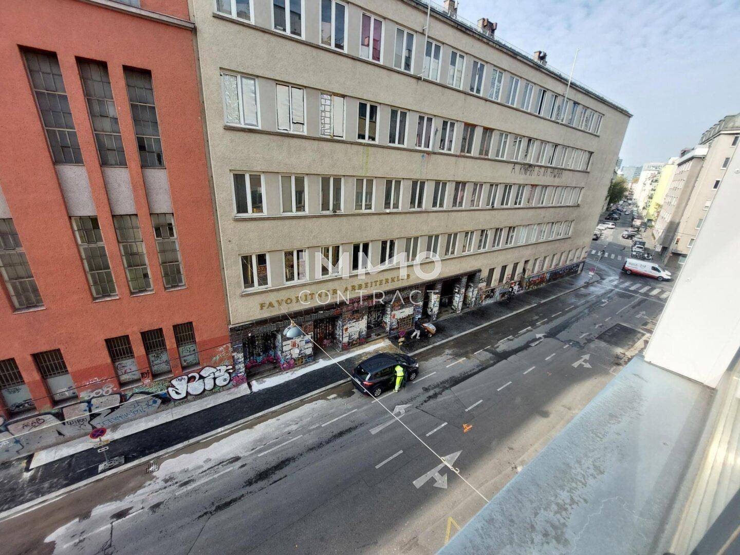 Ansicht eines Mehrfamilienhauses an einer belebten Straße mit Geschäften im Erdgeschoss.