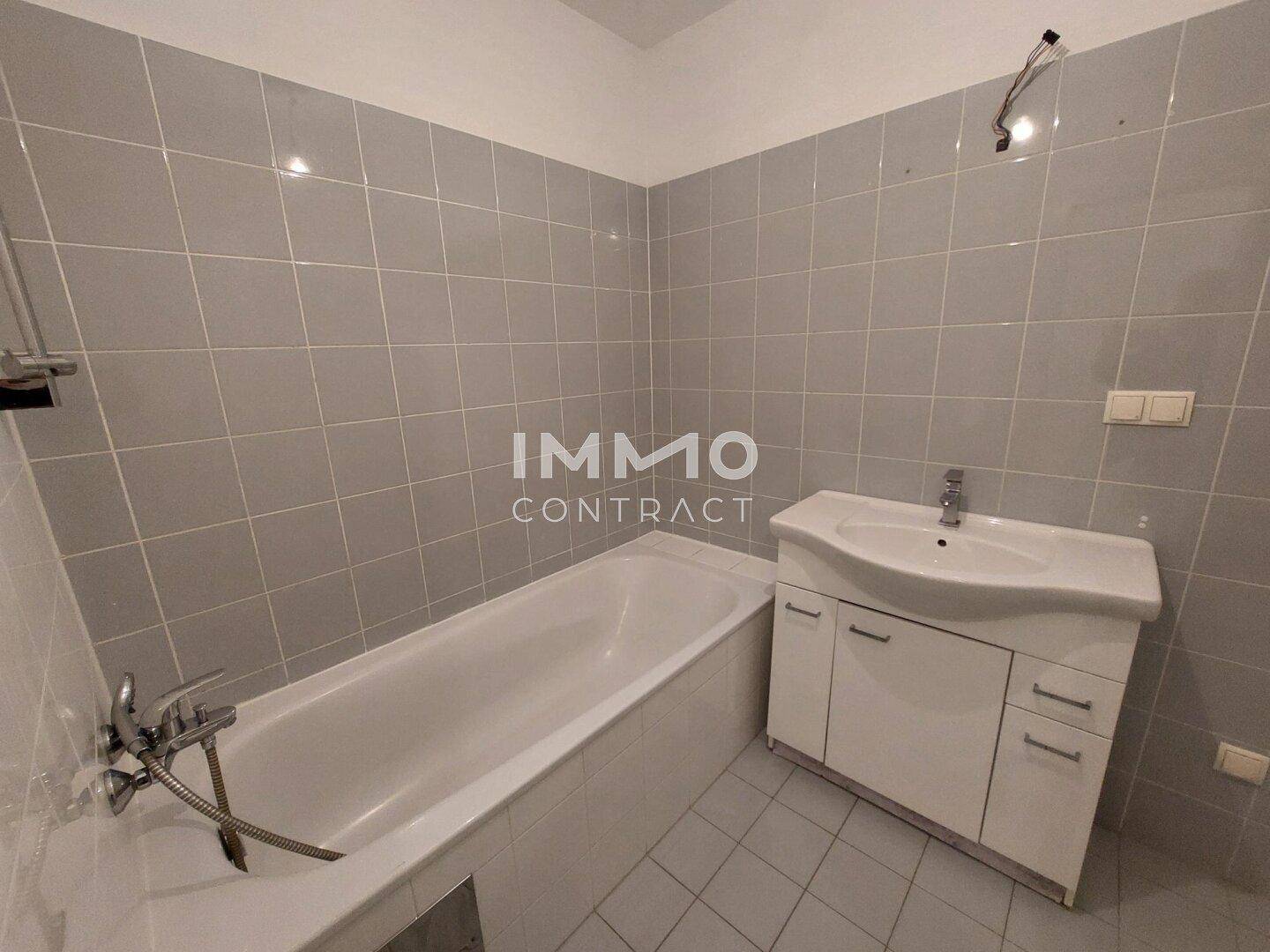 Badezimmer mit Badewanne, Waschbecken und hellgrauen Wand- und Bodenfliesen.
