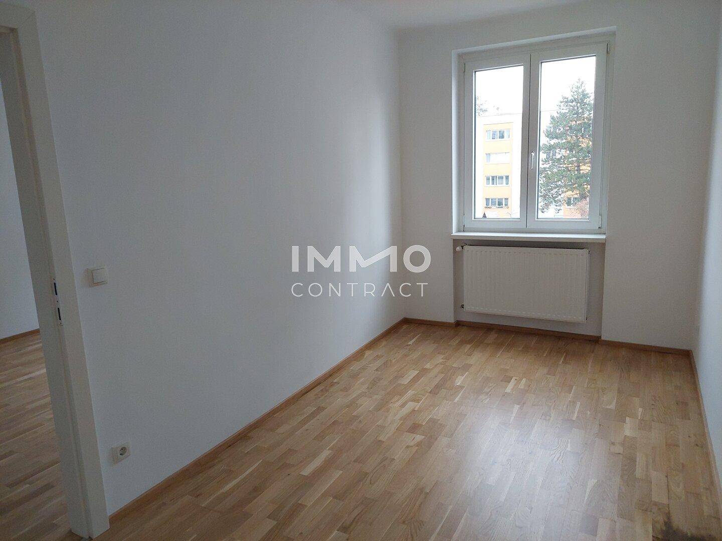 Geräumiges, leeres Zimmer mit Parkettboden und Fenster, ideal als Schlafzimmer.
