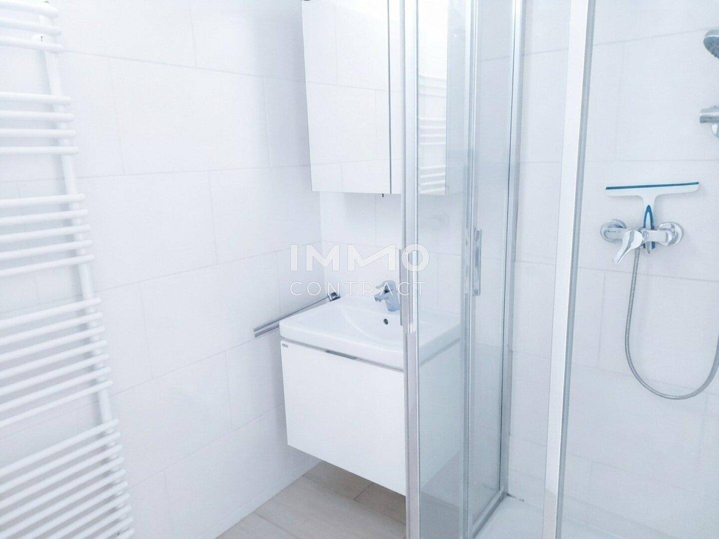 Modernes Badezimmer mit weißen Fliesen, Duschkabine und beheiztem Handtuchhalter.