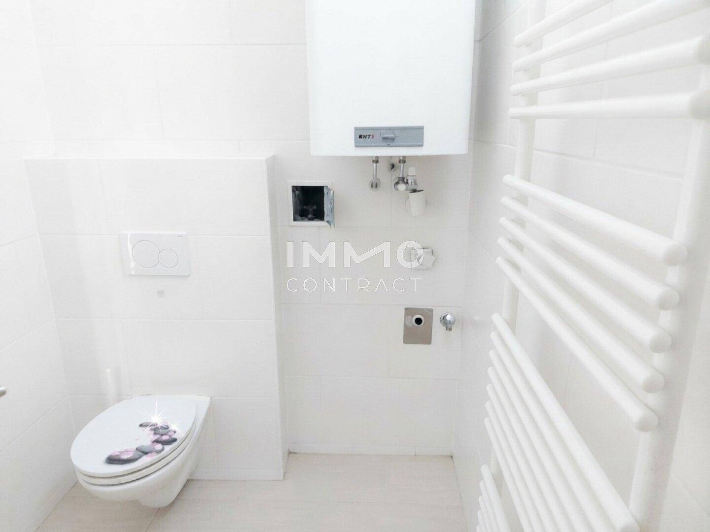 Helles WC mit wandhängender Toilette, Warmwasserbereiter und beheiztem Handtuchhalter.