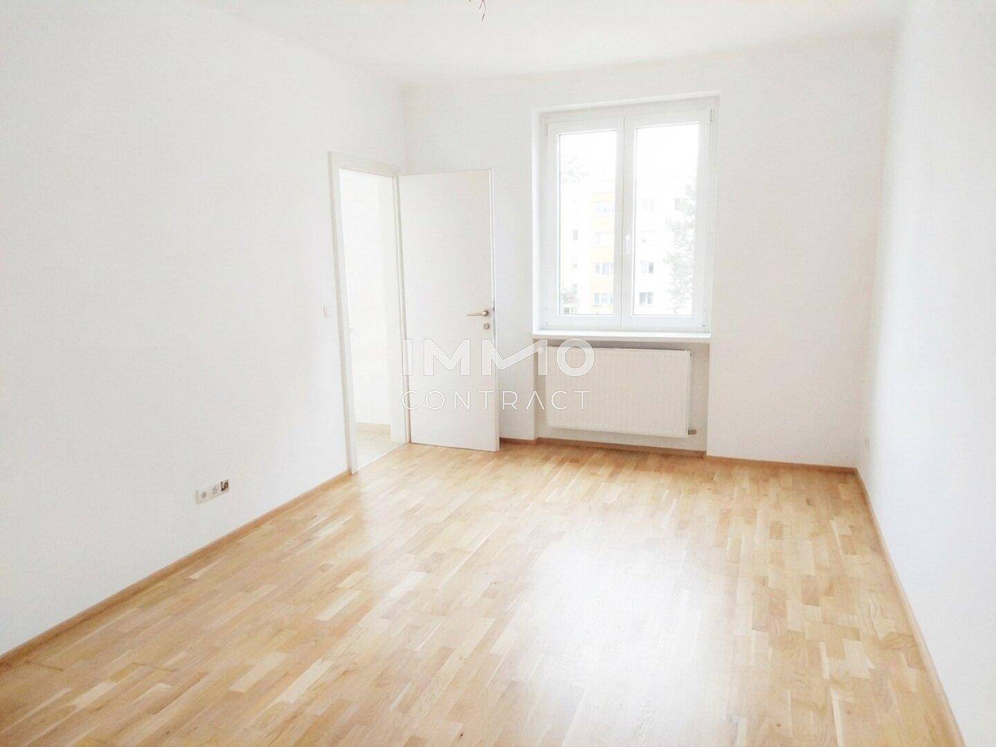 Leeres Zimmer mit Parkettboden und Fenster, das viel Tageslicht hereinlässt.